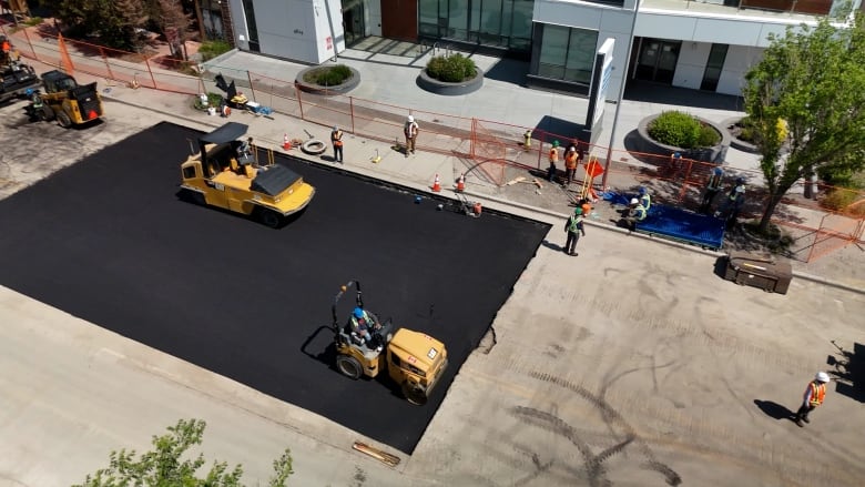 a road with construction workers, equipment, and fresh asphalt.