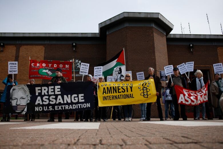 A line of protesters holding signs in front of the brick wall outside a prison.