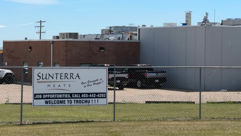 A sign is pictured that reads Sunterra Meats outside of a fence near a building.