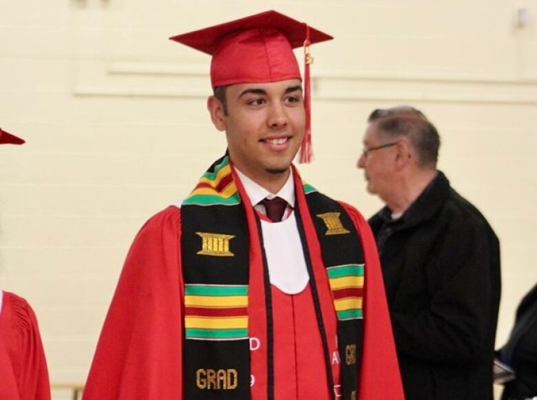 A young man is shown in a red gradudation outfit.