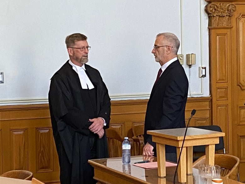 A man wearing a suit speaks with another man wearing a legal gown.