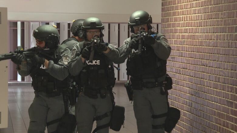 Four police officers wearing tactical gear and holding carbine rifles fan out through the hallway of a school during a training scenario.