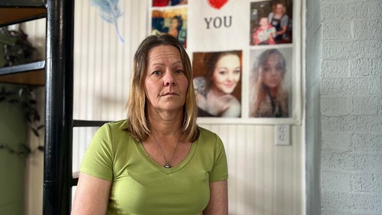 Woman in a green T-shirt sits in front of a wall that features photos of a younger woman and the caption 