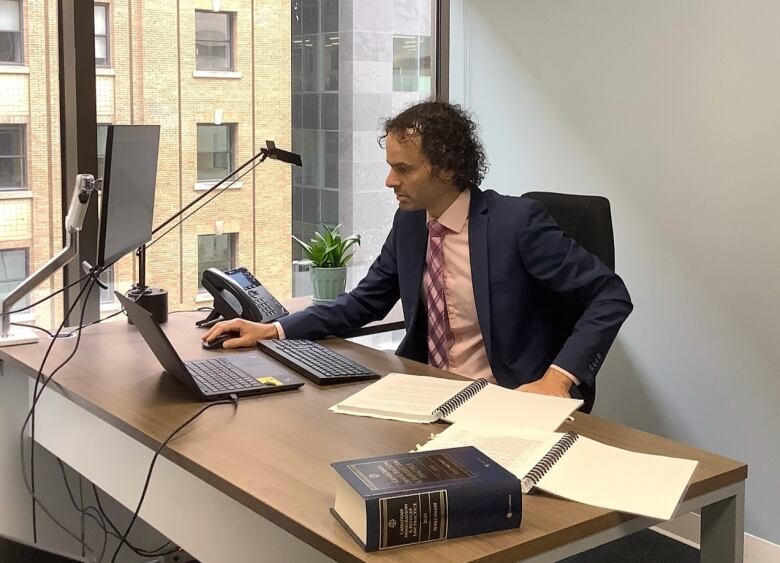 A man at an office desk looks at a laptop.