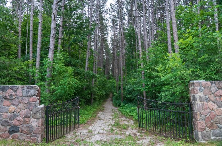 A black gate opens up to a path, green foliage and tall trees leading into the new Uxbridge Urban Provincial Park.