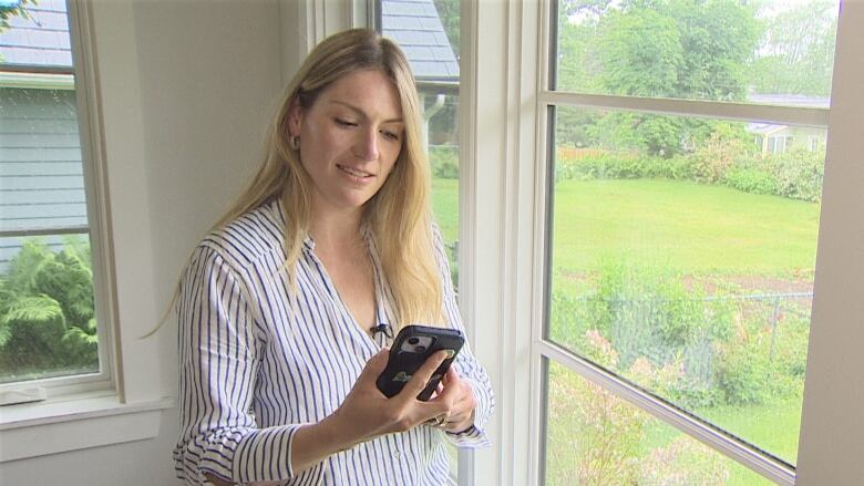 Sarah Blanchard-Eng stands near a window in her home, holding her cellphone.