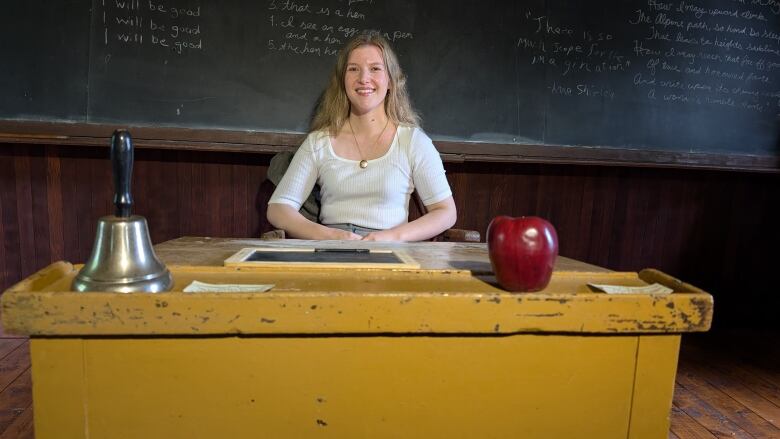 A woman sits at an old-fashioned desk with an apple on it 