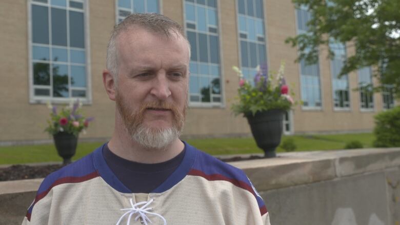 Man with beard and somber facial expression wears hockey jersey.