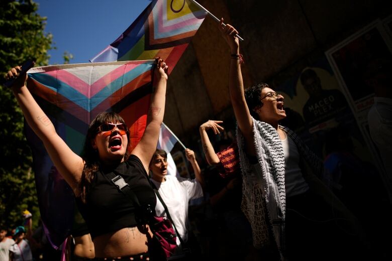 People chant and hold up flags during a Pride parade.