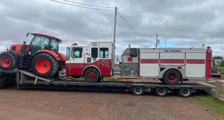 A fire truck loaded onto a flatbed truck for transport along with another piece of heeavy equipment.