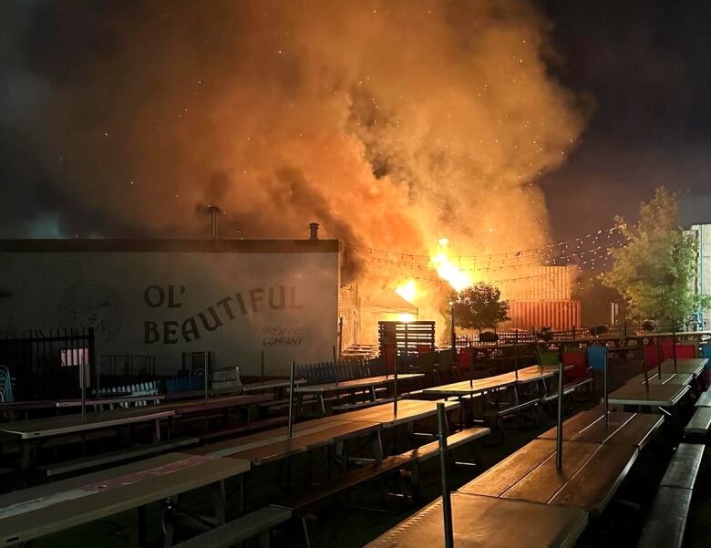 Photo shows a large orange flame beside a building in the night. 