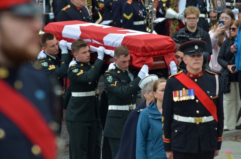 Military members carrying a casket draped in a Canadian Flag. 