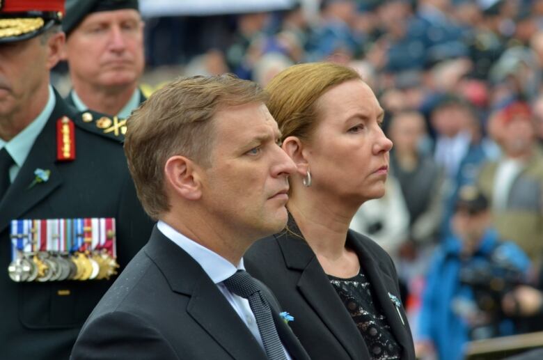 A man and a woman wearing black stand in front of a military member. 