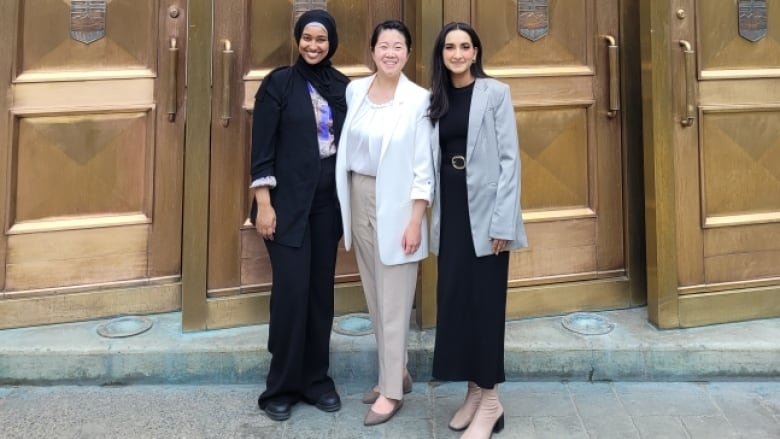 Three women stand in front of the decorative bronze doors of the Calgary Courthouse.