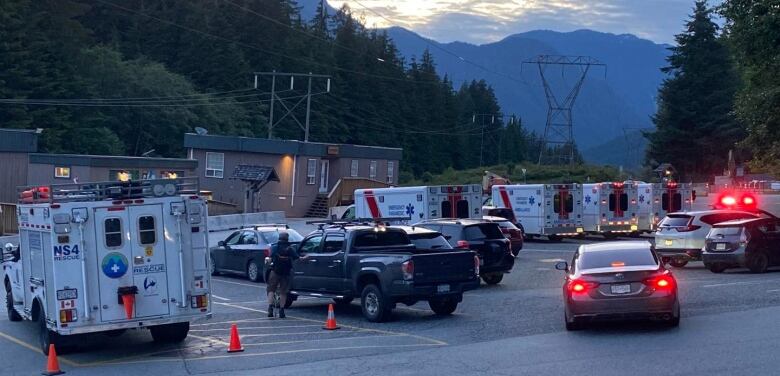 ambulances wait in a parking lot, an evening sky and lowrise building is behind them