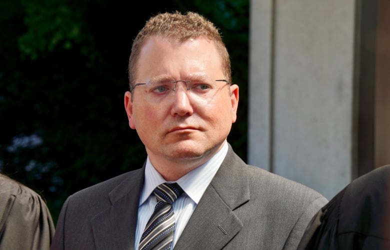 A man in glasses and a suit outside a courthouse on a summer day.