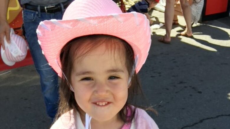 A little girl in a pink cowboy hat, smiling.