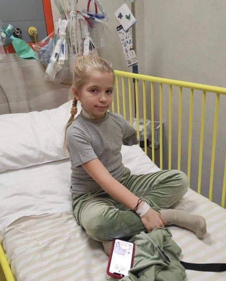 Blond girl sits in hospital bed with amputated arm