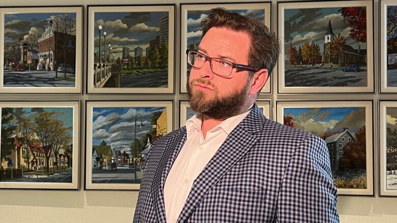 A man in a white shift and checked jacket stands in front of a wall of colourful prints