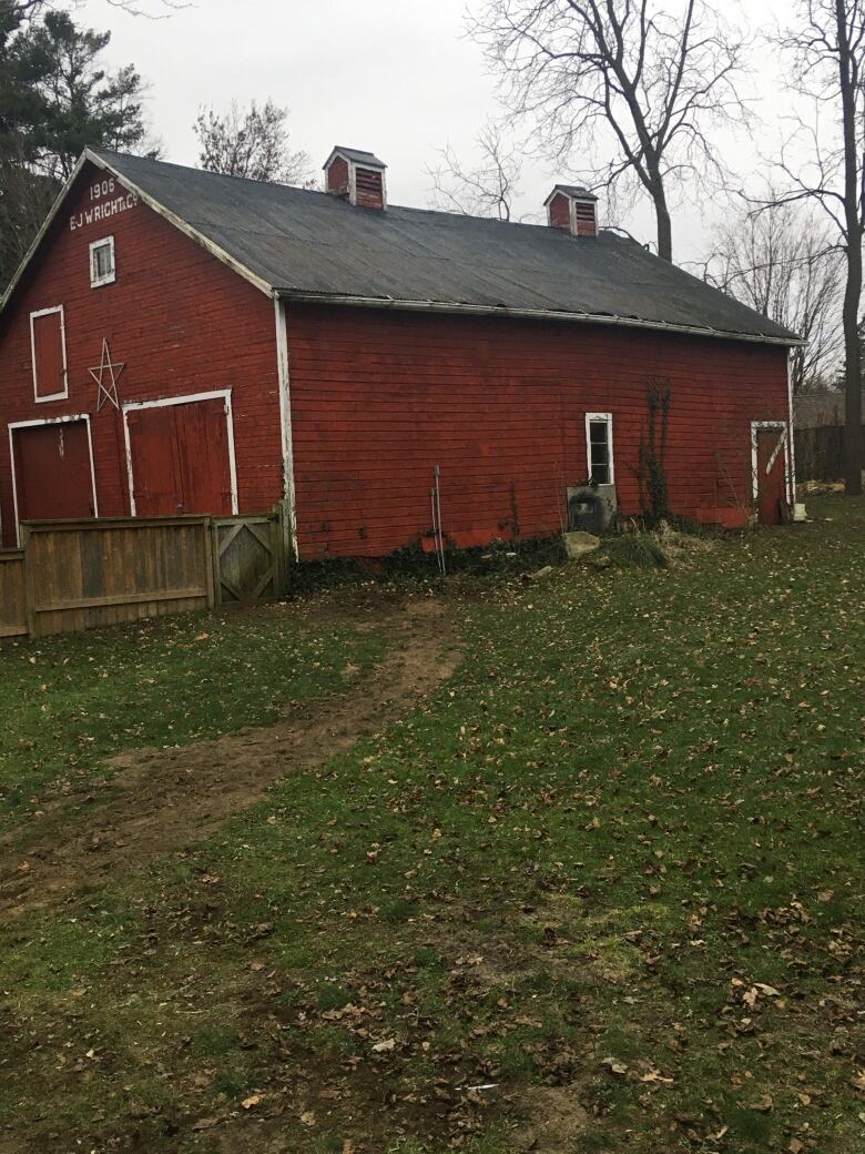 A photo shows an old, red barn sitting on green grass.