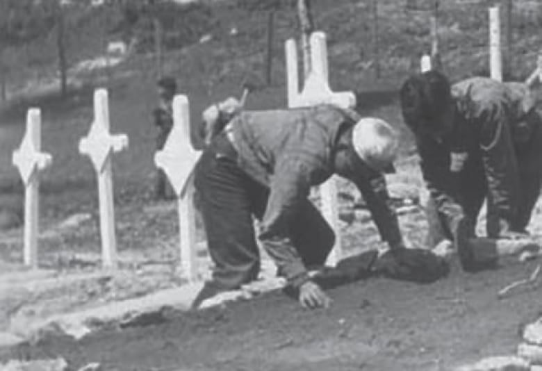 Youth are kneeling over, and possibly tending to, a grave in the Kenora residential school cemetery.