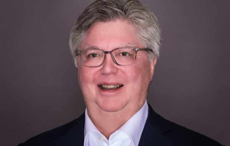 A man with a full head of grey-white hair and glasses.