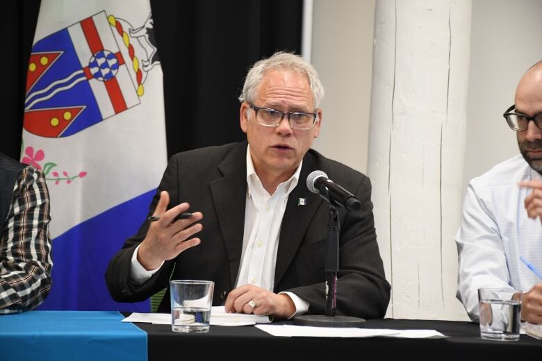 A man in a suit gestures while speaking into a microphone.