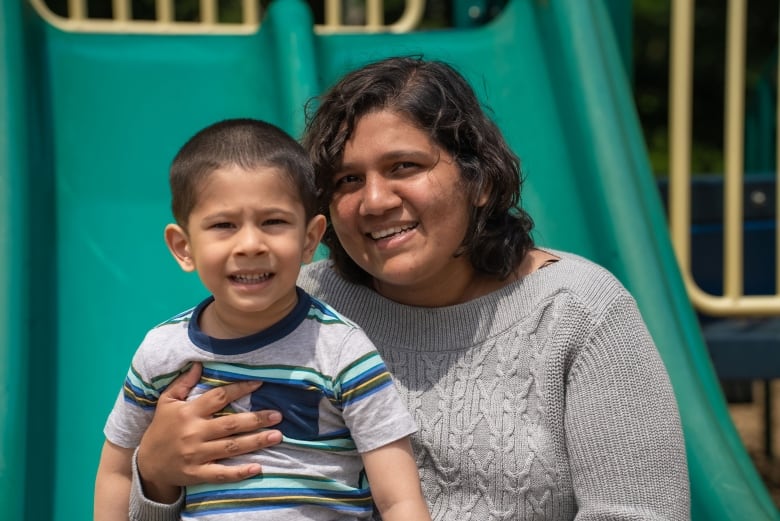 Woman holds her toddler son on a slide.