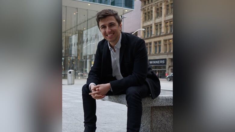 A man in a suit sits in a downtown square. 