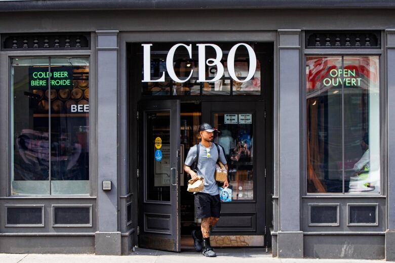 A man leaves a liquor store with alcohol in his hands.