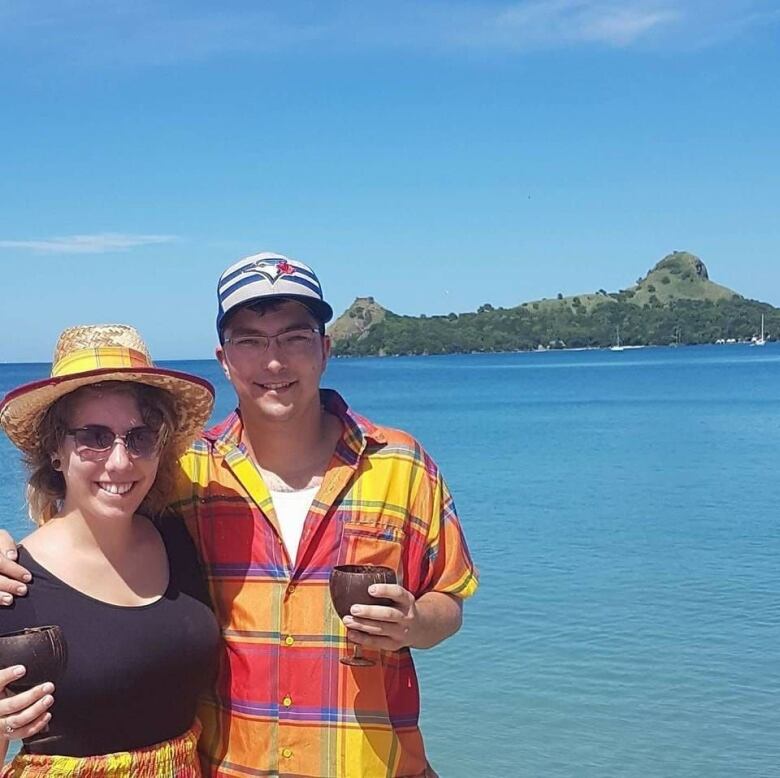 Two people wearing hats posing in front of a body of ocean.