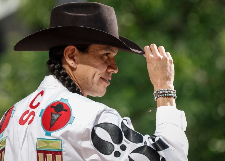 a man in a white shirt wearing a cowboy hat touches the hat