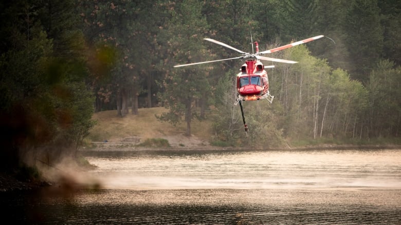 A helicopter with a bucket gets water from a lake.