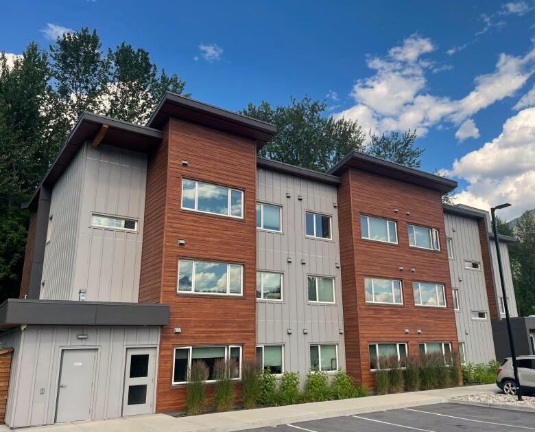 A 24-unit housing complex is photographed against the backdrop of trees and blue sky.  