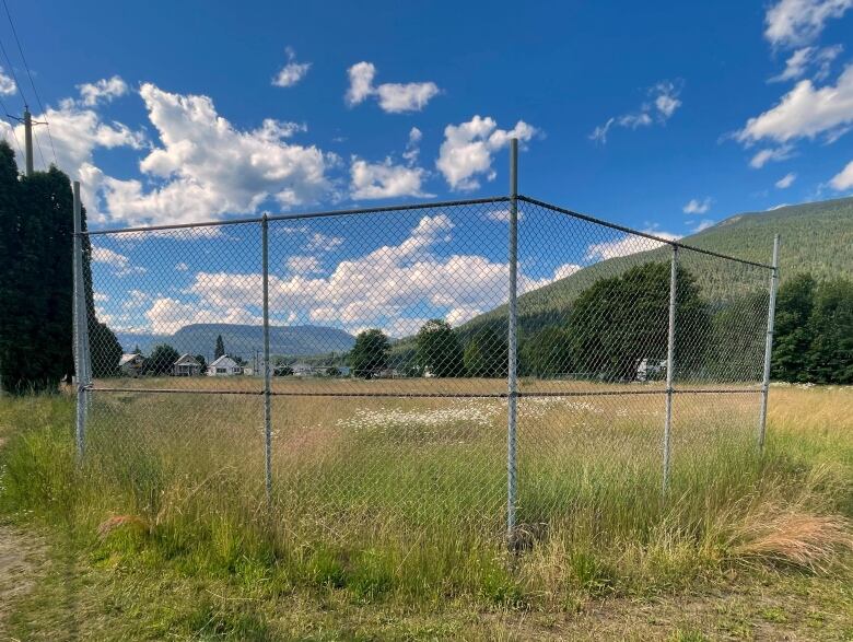 A fenced off patch of green field with verdant hills and smattering of houses seen in the background.