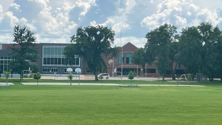 A wide green lawn and basketball nets in front of a school