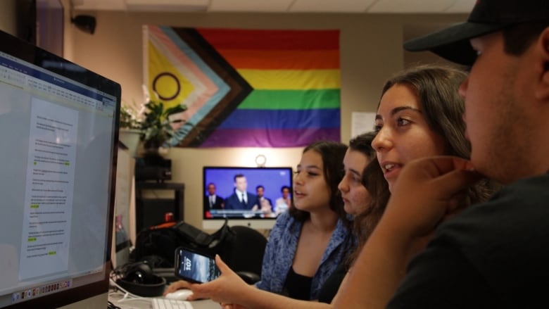 Students look at a computer screen together at a desk. 