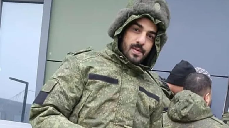 A man in a camouflage hooded jacket looks at the camera.