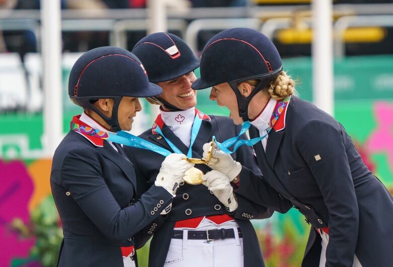 Three women in equestrian outfits holding gold medals