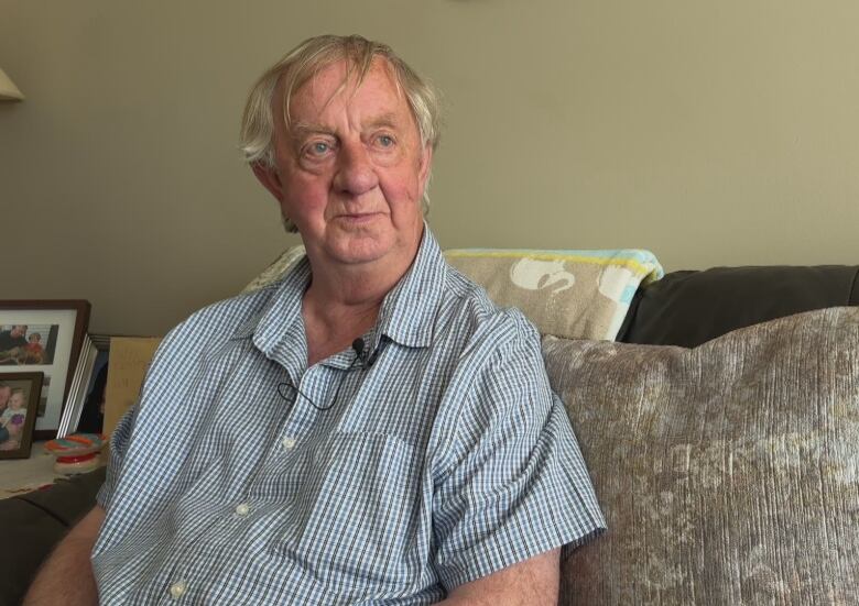 An older man with a short-sleeve shirt sits on a couch. 