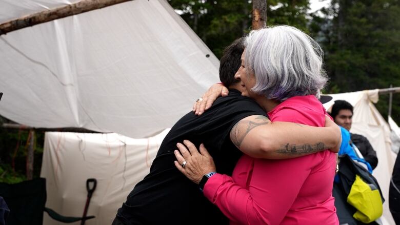 Two women hug in front of a white tent. 