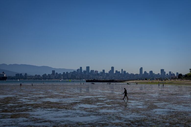 People walk on the beach during low tide as sail boats pass in Vancouver, July 7, 2024. Heat warnings have been put in place for the Metro Vancouver area for elevated temperatures. 