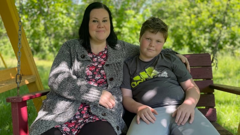 Shirley-Ann Muncey and her son Xavier sit outside on a bench, and look straight at the camera. 