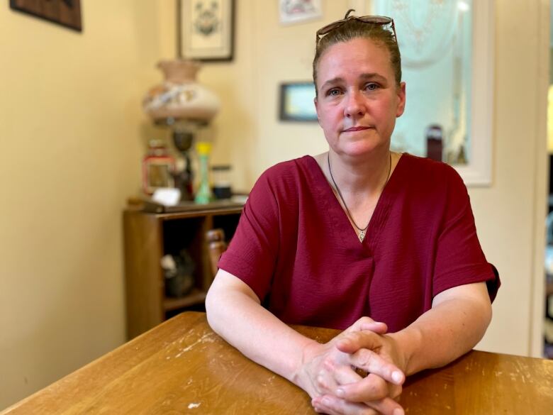 Krista MacGillivray sits at a kitchen table, with her hands folded in front of her. 