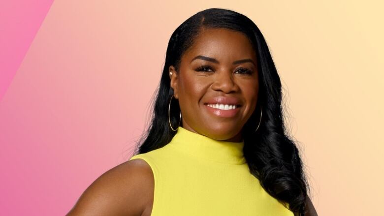 A Black woman with long hair wearing a yellow dress against a pink background. 