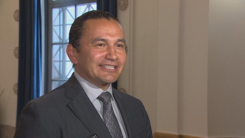 A man in a black suit and black checkered tie stands in a room.