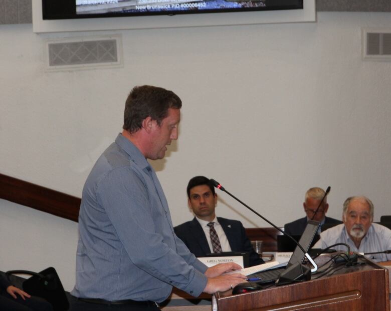 Man, standing at podium, pictured from side, making a presentation.