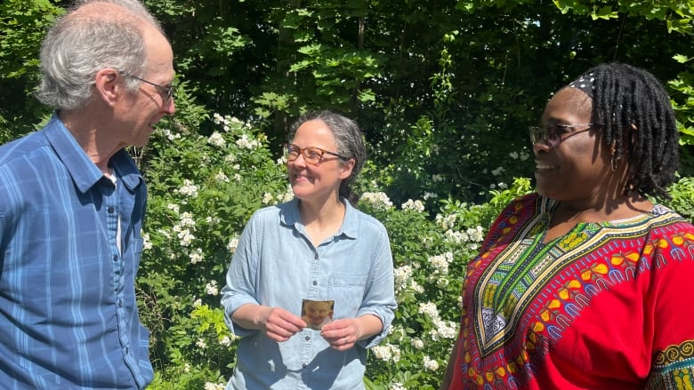 Three people stand in a green garden, holding a phot and laughing at memories. 