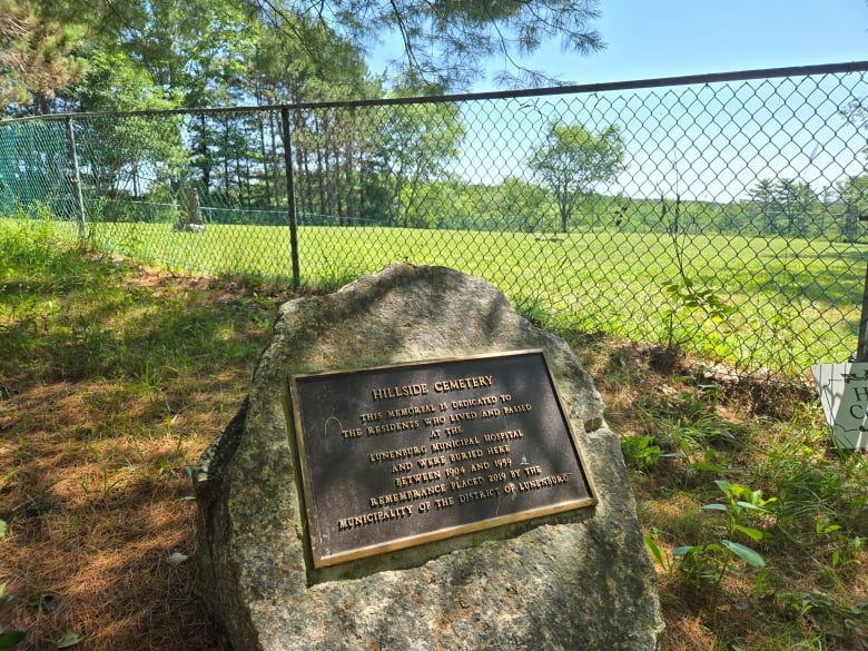 A plaque on a large rock sits outside a fenced-in area.