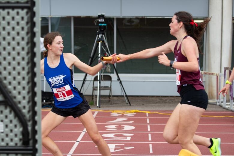 A runner passes another a baton on a track.